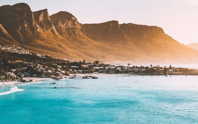 The Twelve Apostles mountain range glowing gold above the turquoise water and white beaches of Camps Bay