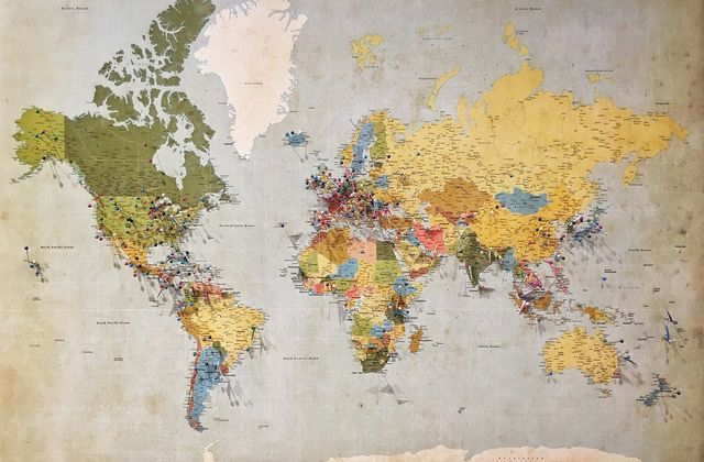 A worn paper world map spread flat, its continents coloured in faded greens and yellows