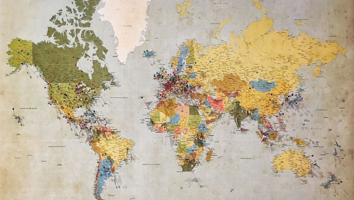 A worn paper world map spread flat, its continents coloured in faded greens and yellows