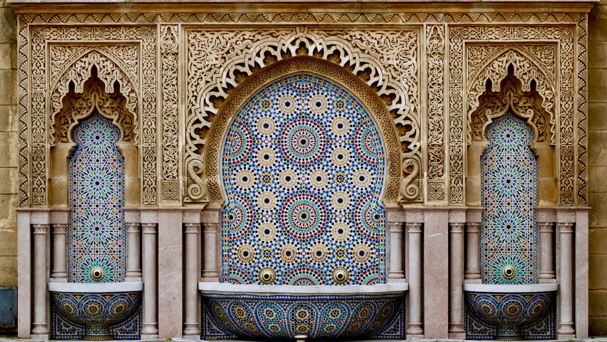 A tiled fountain framed by carved plaster arches in the courtyard of a Marrakech riad