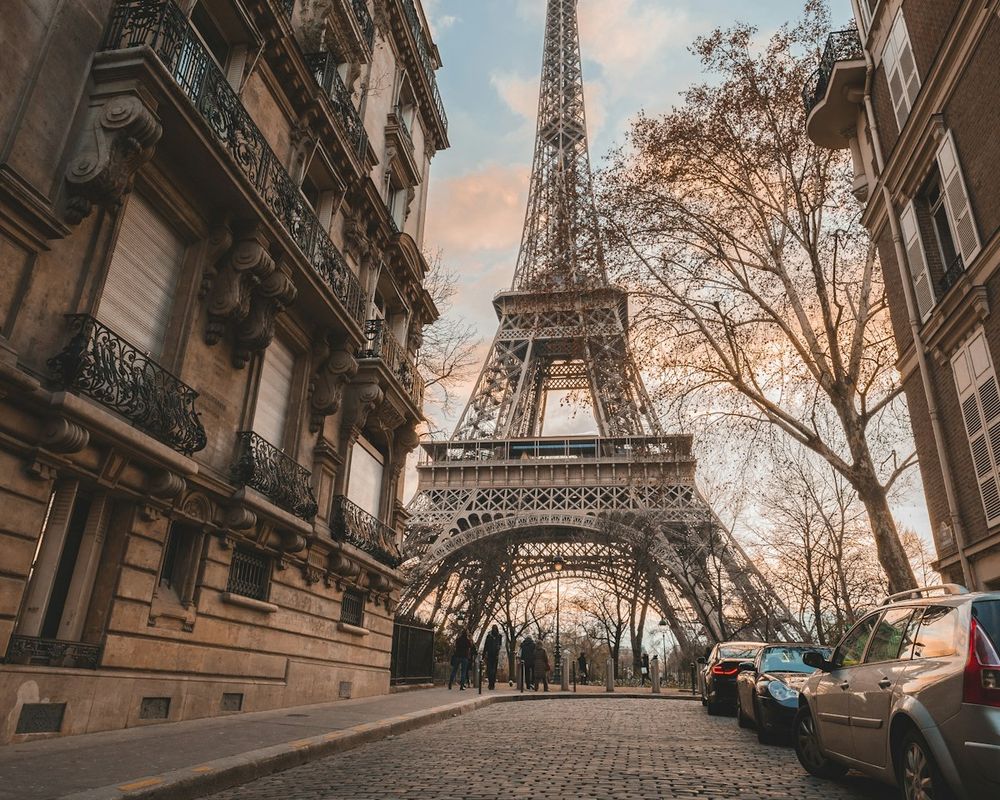 A cobbled Paris street lined with stone apartment buildings, the Eiffel Tower rising at the end