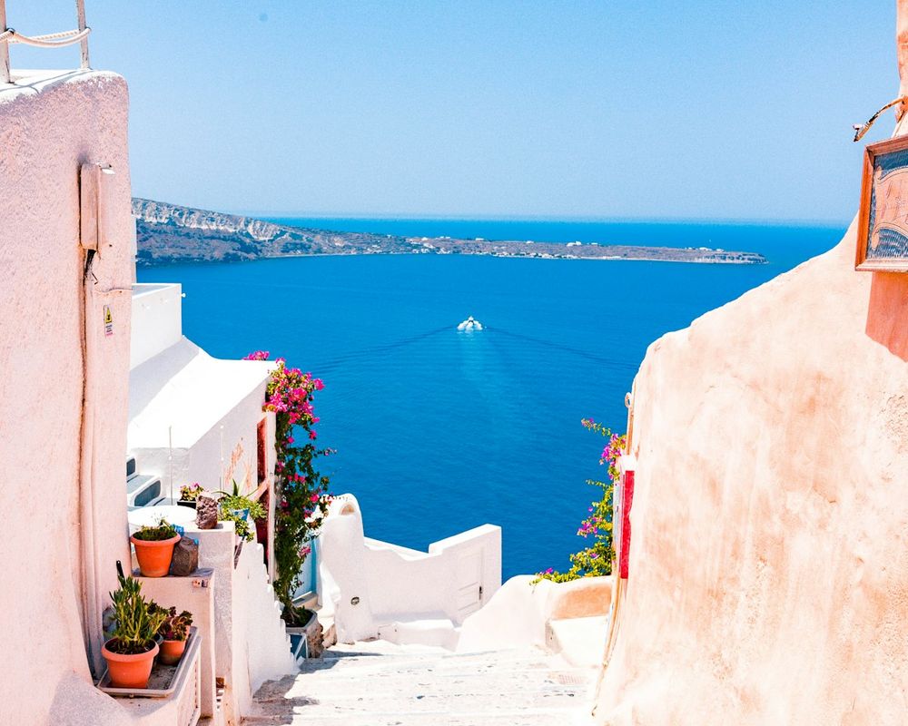 White-washed steps in Oia lead down between pink and white walls to the deep blue Aegean