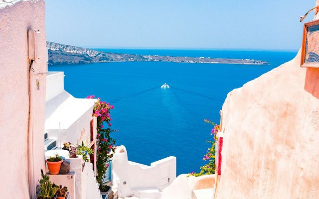 White-washed steps in Oia lead down between pink and white walls to the deep blue Aegean